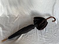 Side view of closed black umbrella with wooden handle and tip, showing the fur embellishment.
