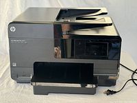 Front and side view of black HP OfficeJet Pro 8160 with automatic document feeder and output tray, placed on a white surface with power cord visible.