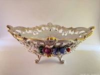 Side view of the large vintage Dresden porcelain pierced footed bowl highlighting the intricate pierced lattice design and gold-tone accent along the rim, with colorful floral appliques.