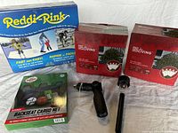 Lot items shown together: Reddi-Rink ice rink kit box, two boxes of For Living clear net lights, hose nozzle, rear seat cargo net box, and solar garden light stake.