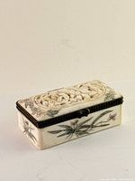 Small rectangular box with carved floral and bird design on the lid, hand-painted floral motifs on all sides, metal trim and clasp visible.