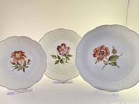 Three decorative porcelain dishes with floral hand-painted designs and scalloped embossed edges, arranged side by side showing front details.