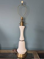 Front view of vintage table lamp showing white milk glass body and brass base, harp, and finial