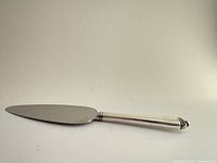Side view of the vintage cake server showing tapered flat blade and sterling silver handle with decorative end detail.