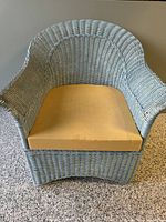 Front angled view of vintage wicker armchair painted light blue with foam seat cushion