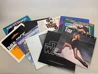 Ten vintage vinyl record albums spread out overlapping, showing various covers including Tina Turner, Grease, Star Wars, and Paul Simon with readable titles and artist names.