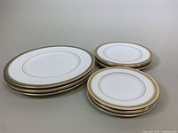 Set of 12 bone china plates grouped in three stacks representing dinner plates, luncheon plates, and dessert plates with clear gold trim around edges.