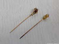 Full view of two 14K and 10K gold pins with decorative stones on white background.