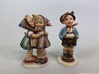 Two vintage Goebel porcelain figurines in good condition: a singing boy and two girls hugging.