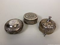 Three antique European repousse metal trinket boxes arranged side by side showing overall detail, shape, and size.