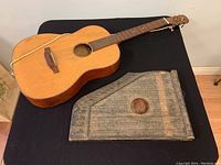 Photo of vintage acoustic guitar and antique wooden zither side by side on black cloth background