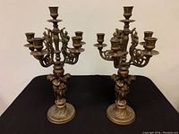 Pair of brass six-arm candelabras with cherub bases on a black surface.
