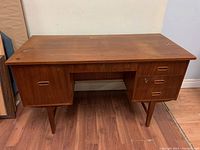 Front view of mid-century Danish teak desk showing drawers, cabinet, and angled legs