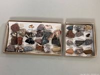 Two boxes of natural rock crystals and semi-precious stones shown from above. Stones vary in color, shape, and size. Labels present beneath each stone.