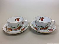 Pair of porcelain Evesham fruit pattern teacups and saucers shown side-by-side on flat surface.