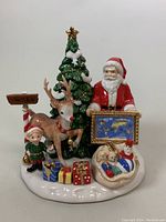 Front view of the Royal Doulton Santa figurine showing Santa holding a framed world map, Christmas tree, reindeer, elf, gifts, and snowman.