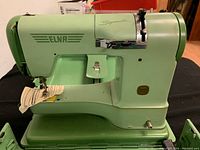Front view of aged green ELNA Supermatic sewing machine mounted on base with fabric piece under needle.
