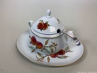 Soup tureen with lid fitted with ladle, showing fruit motif decoration and gold trim.