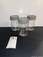 Three vintage glass jars with metal screw-on lids, placed on a black surface with a white backdrop, showing front and side views.