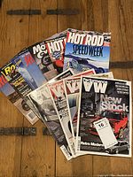 Photo showing 10 car and motorcycle magazines spread out on wooden floor, including Hot Rod, Performance VW, and other automotive titles.