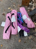 Four children's folding camping chairs in carrying bags placed on ground, three pink and one purple with star pattern visible.