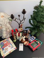 Photo showing the artificial Christmas tree and a selection of boxed and loose ornament decorations, a metal candle holder, and a Santa figurine in festive attire.