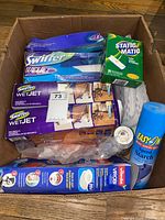 Box containing Swiffer WetJet pads, Vileda microfiber pads, Static Matic pads, Easy On starch spray, and other cleaning accessories.