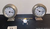 Wide shot showing the two matching round chrome clocks and the airplane clock in the center, all with white faces and Roman numerals.