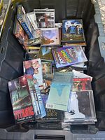 Overview photo showing DVDs, CDs, and VHS tapes including Titanic, Harry Potter, and various music albums in a black plastic container.
