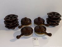 Full set of escargot plates and French onion soup bowls with lids arranged on white surface