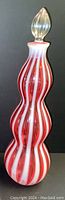 Tall Fenton glass bottle with red and white twisted stripes and clear glass stopper on dark background