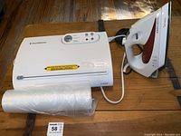 FoodSaver vacuum sealer with roll of sealing bags and Black & Decker iron on wooden floor.