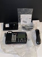 Bell 390 corded landline phone with handset, base, power cord, and manual laid out on black background, wrapped in plastic packaging