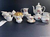 Mini tea sets with multiple small porcelain pieces including teapots, creamers, sugar bowls, and trinket box, all decorated with floral patterns and gold embellishments against dark background.