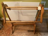 Wood quilt rack showing front view with two horizontal bars and turned wood posts on each side. Missing top piece on one side.