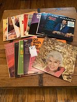 Photo of the full collection of approximately 17 vinyl record albums spread on a wooden surface. Visible album cover titles include Jerry Vale, Andy Williams, and others.