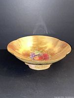 Front angle view showing the bowl's fruit motif and scalloped edges on a golden brown background.