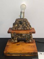 Full view of the handmade lamp with light bulb mounted on top of a stone-covered body sitting on a reddish-brown wooden base.