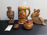 Front view of all five items against plain background: ceramic stein, carved wooden man figurine, abstract wooden couple figurine, wooden sugar container, small wood box