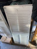 Pair of white wood louvered window shutters stacked, showing the slats and tilt rod mechanism.