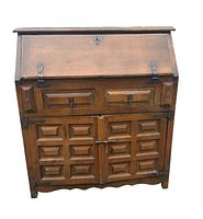 Front view of the antique solid oak country bureau showing the drop-front writing surface, two drawers, and carved cabinet doors with metal hardware.