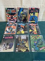 Image showing nine Batman comic books from DC Comics spread on table with clear covers and recognizable titles and characters.