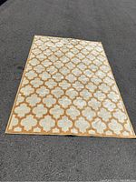 Photo of the DYNAMICRUGS Siena rug laid flat on asphalt showing geometric pattern and light brown and cream colors