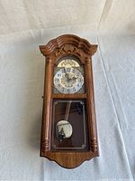 Full view of Hermle wooden wall clock showing decorative top molding and glass panel over pendulum.