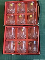 Two open boxes arranged on green cloth showing six short goblet glasses each, twelve total, with original brand stickers on each glass.