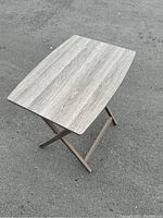 Image showing the tabletop's light gray wood grain texture and rectangular shape with the dark folding X-style base visible beneath.