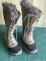 Front and side view of the pair of Sorel women's boots featuring tusk stone leather uppers, black rubber toe area, and grey faux fur lining at collar.