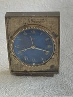 Front view of the vintage Birks desk clock showing the blue dial, gold Roman numerals, and beaded bezel, within the square metal tarnished case