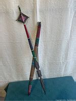 Group of five wooden arrows decorated with Native American style folk art patterns, standing against white lace curtain, showing colorful hand-painted geometric and traditional motifs.