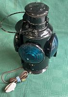 Front and side view of the vintage black metal railway lantern with blue lenses. Electrical cord and inline switch visible on table surface.